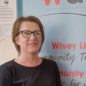 Image shows a white woman smiling in front of a charity branded banner.