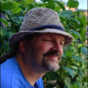 Image shows staff member Neil Gent wearing a blue T shirt and grey hat. He is smiling.